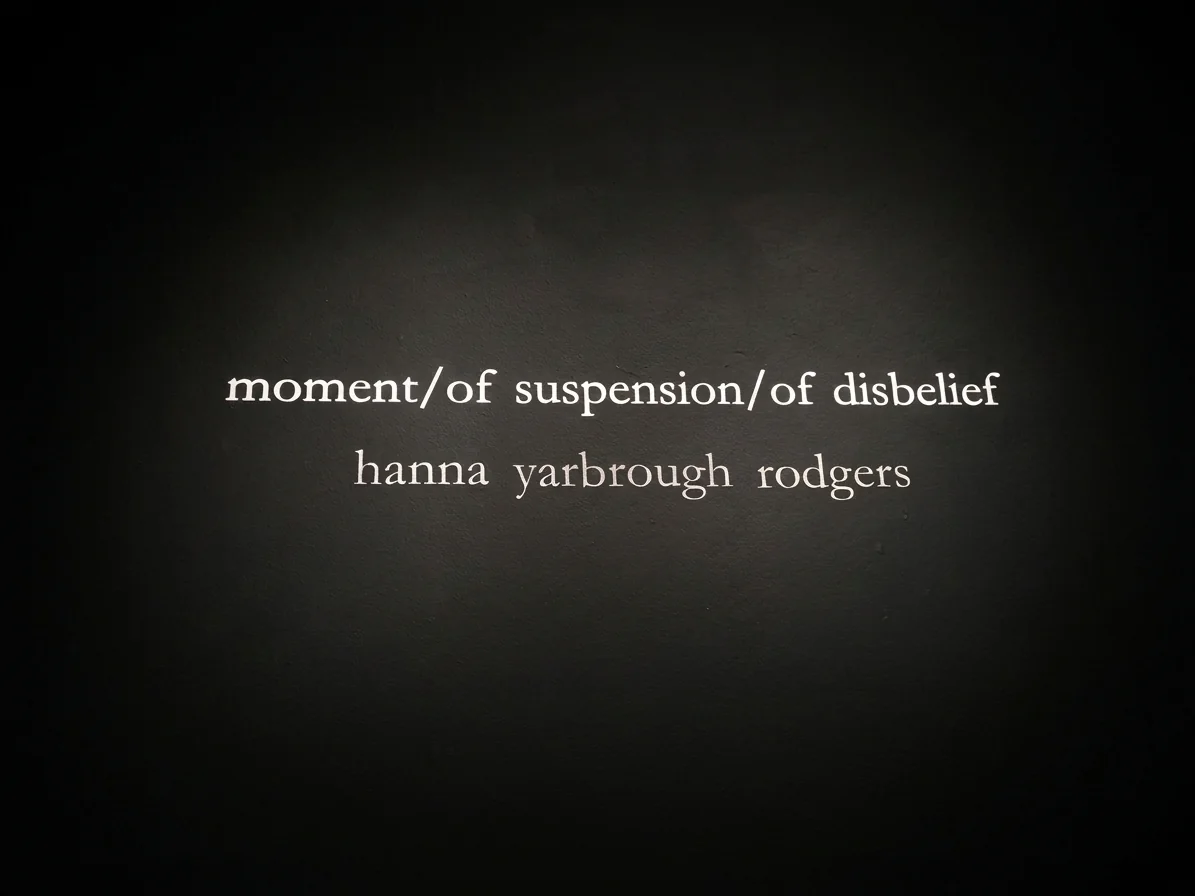 The exhibition title and artist name in white vinyl on the black gallery wall