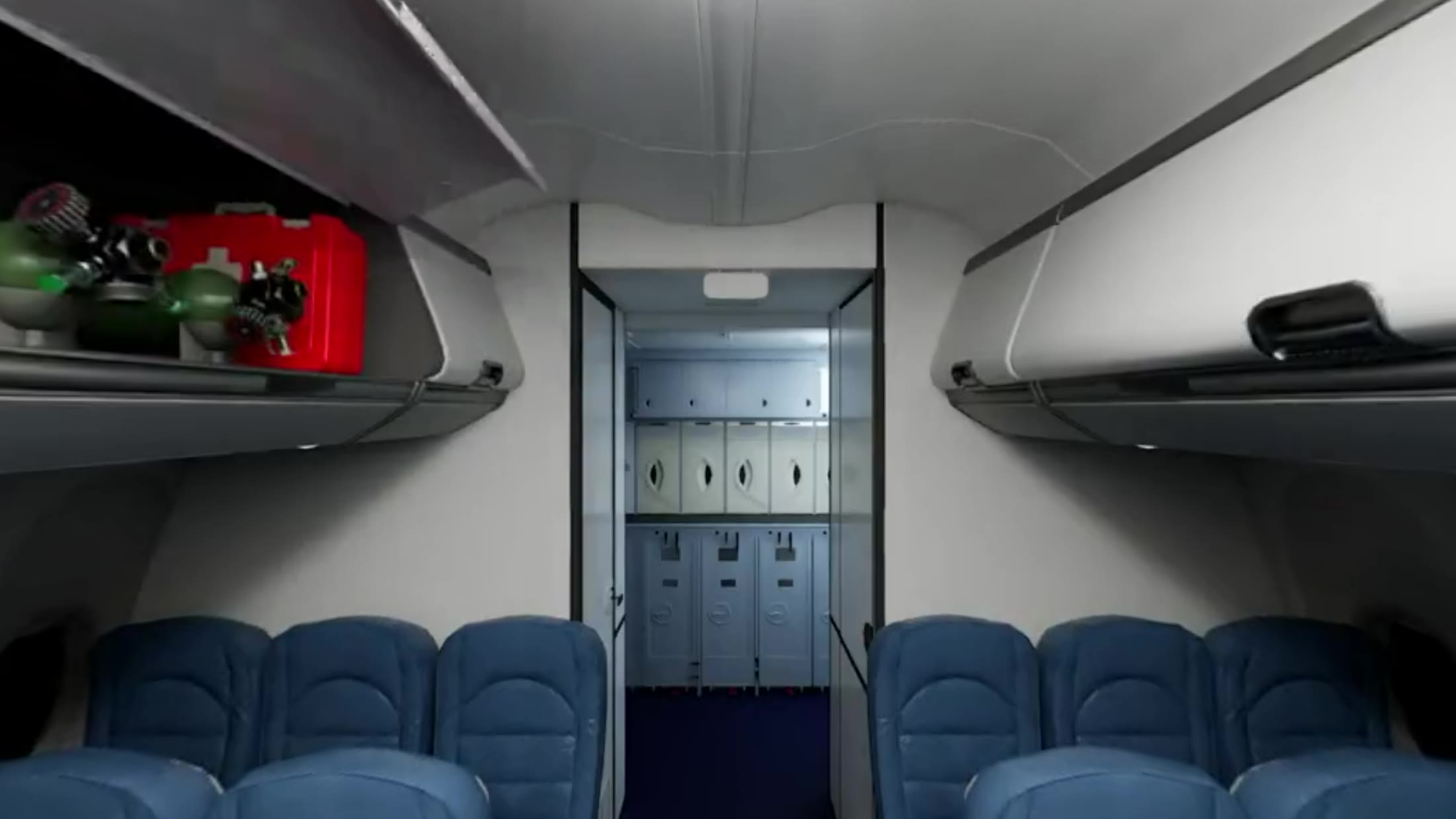 The aircraft cabin interior, looking down the aisle at the emergency oxygen bottle